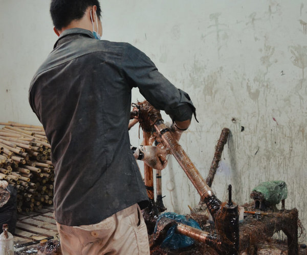 Ein Handwerker umwikelt die Verbindungselemente eines Bambusrahmens mit Hanffasern.